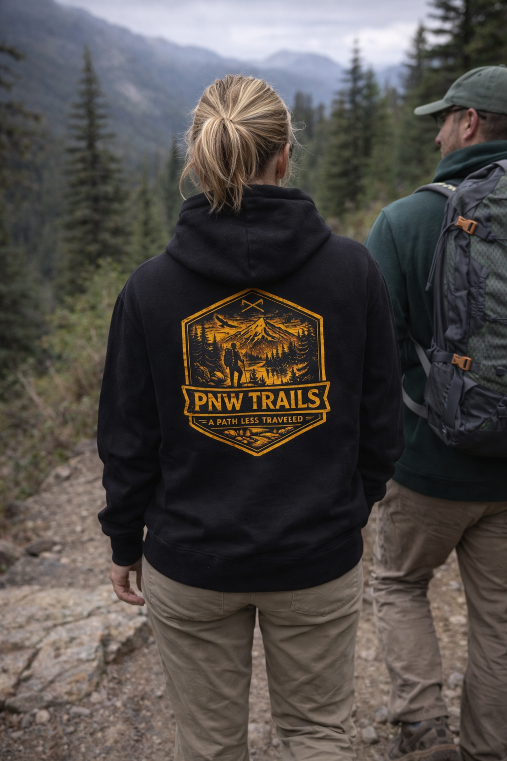 Two people hiking in a mountainous area with one wearing a black hoodie featuring 'PNW Trails' design.
