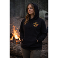 Person wearing a black hoodie with Naughty Goat logo in front of a campfire and tent in a forest setting