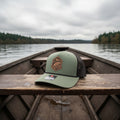 Green baseball cap with logo and text on a wooden bench seat of drift boat