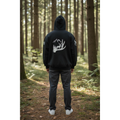 Person wearing a black hoodie with a white graphic in a forest