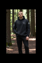 Black hoodie with text and logos in a forest setting
